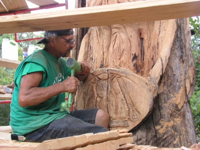Person with tool carving into wood totem sculpture