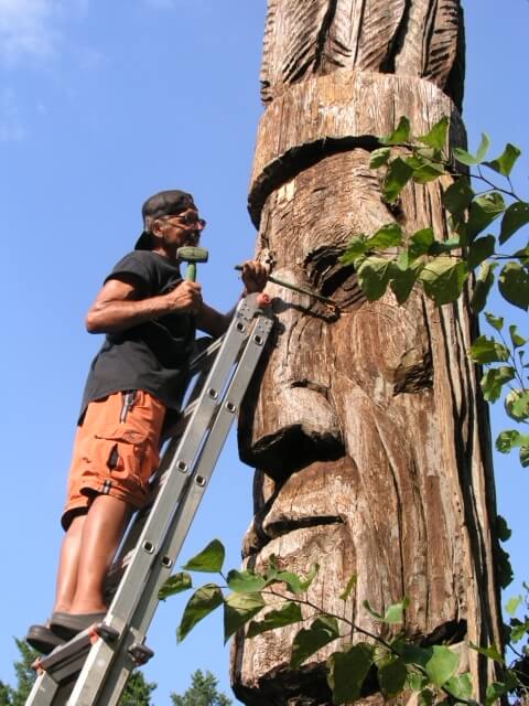 Person on ladder working on wood totem sculpture