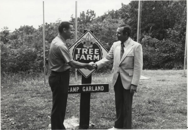 Verdo Hooker and Dale Campbell shaking hands at Tree Farm sign at Camp Garland.